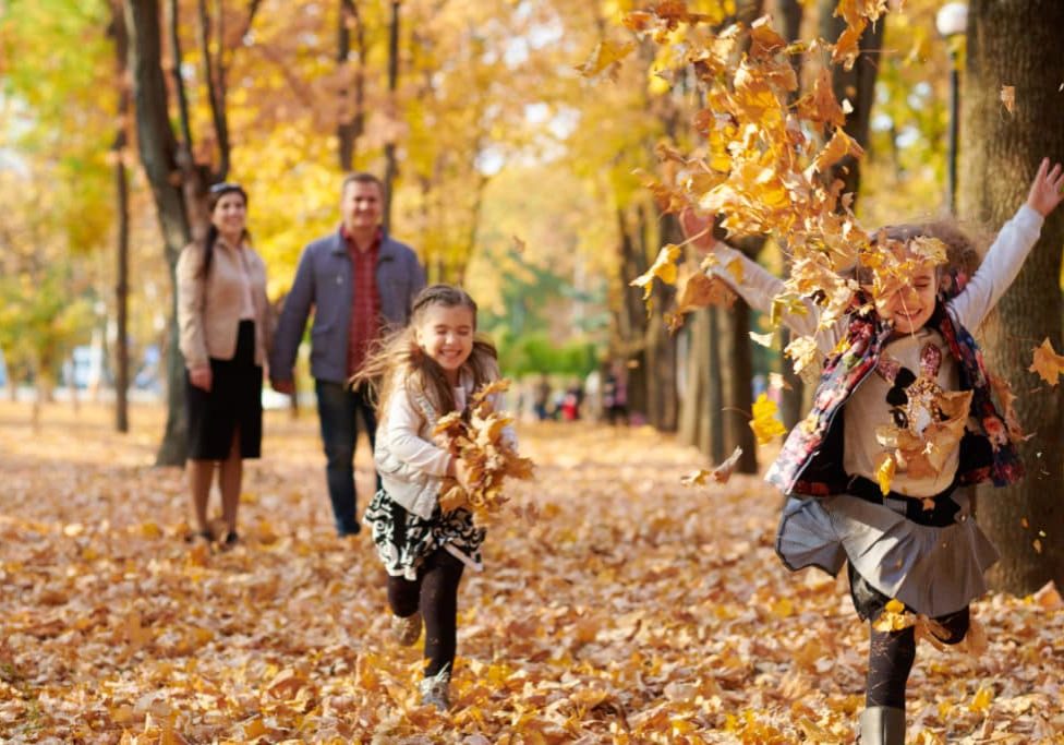 Happy family is in autumn city park. Children and parents running with leaves.. They posing, smiling, playing and having fun. Bright yellow trees.